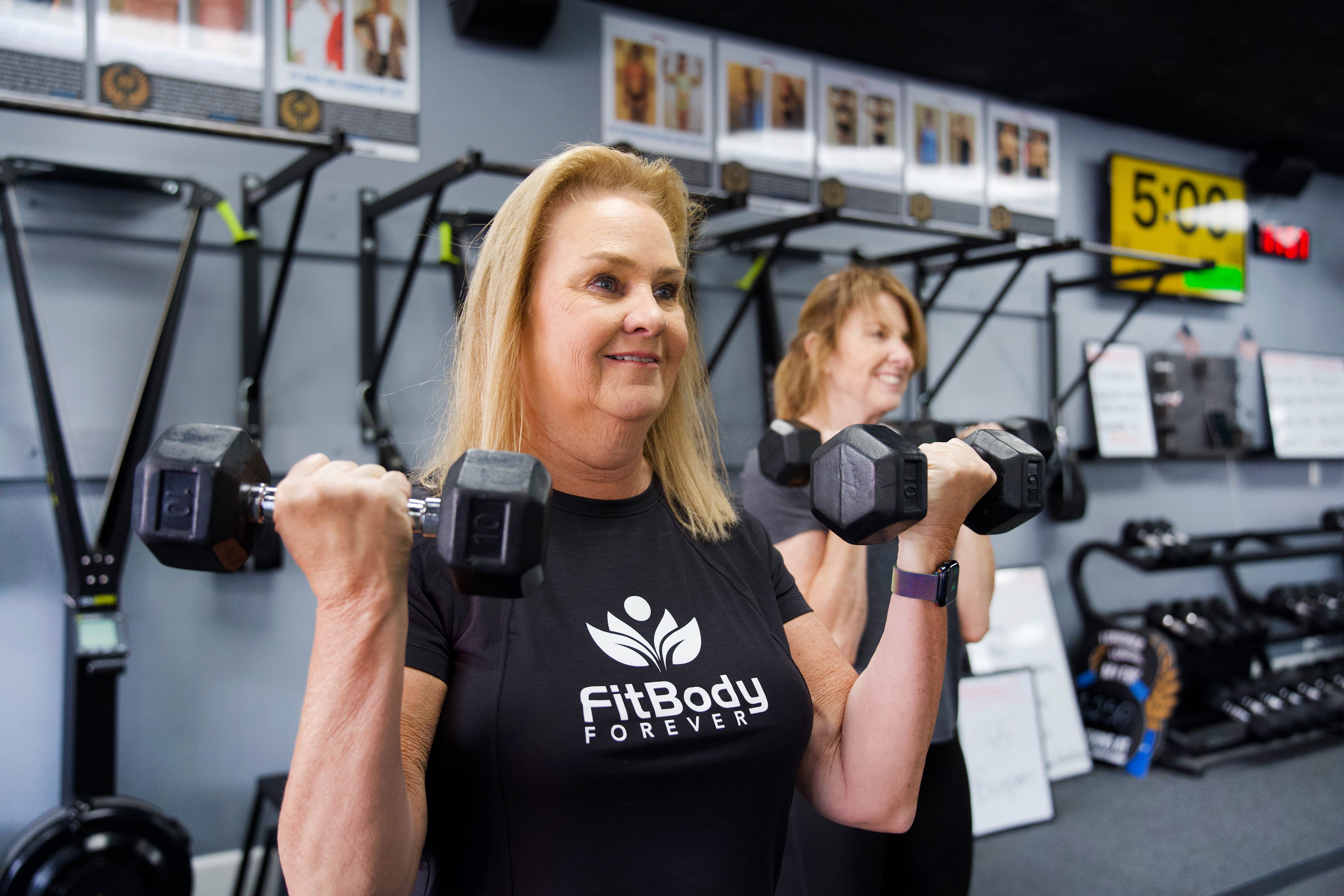 A Fit Body Forever member training with dumbbells and smiling